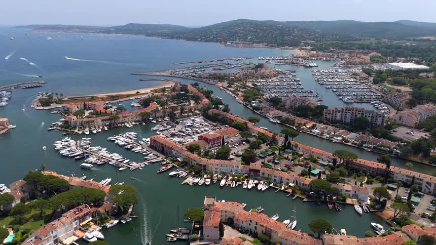 Sweeping aerial footage over a luxurious coastal marina village with canals, waterfront homes, and countless docked yachts