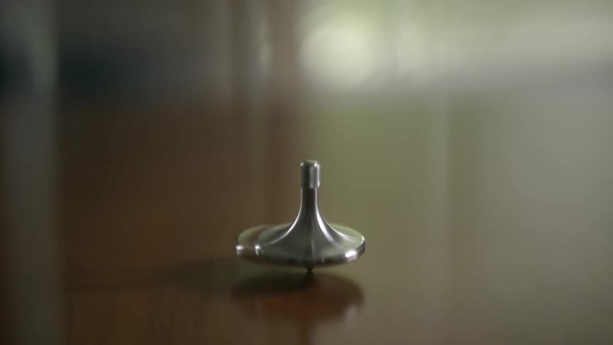 A silver spinning top rotates and wobbles on a polished wooden table in a mesmerizing close-up shot