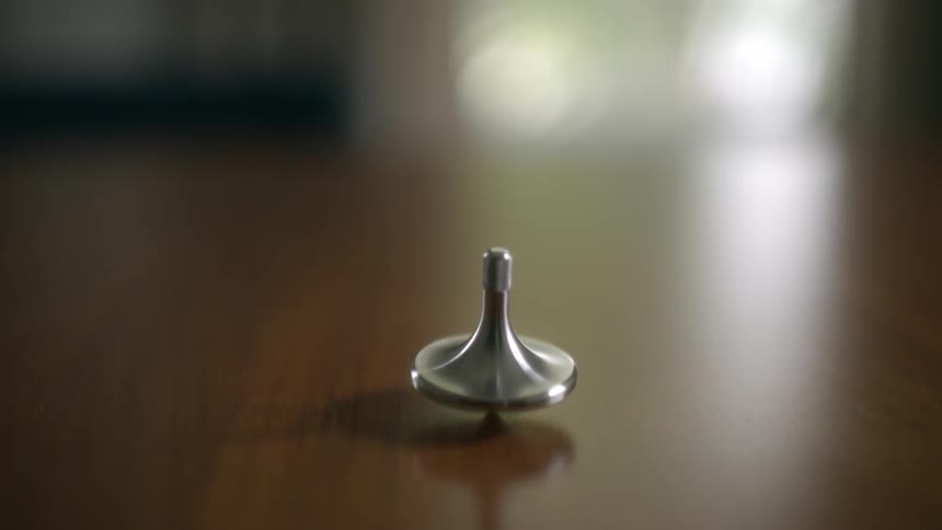 A sleek, metallic top is spun by hand and continues to whirl on a smooth wooden tabletop