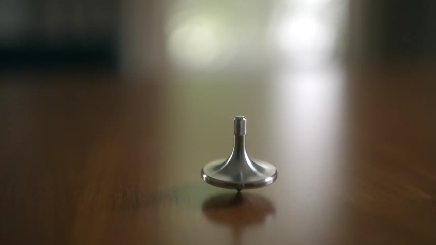 A silver spinning top rotates smoothly on a polished wooden surface with a soft focus background