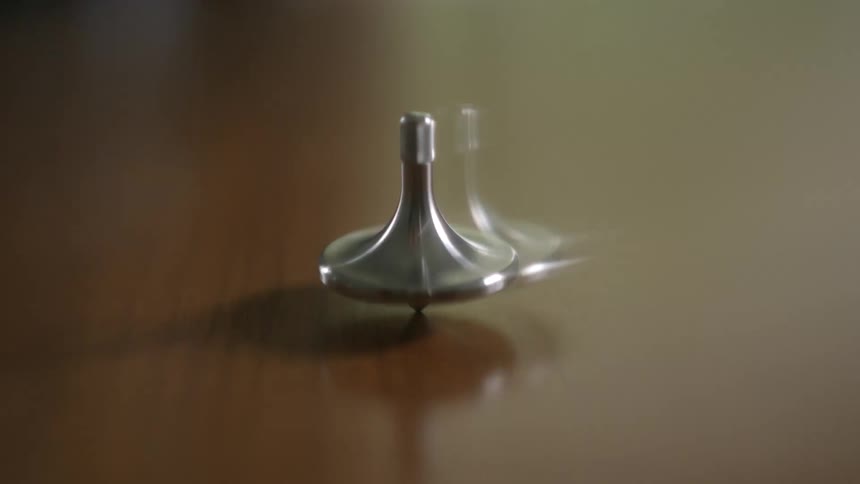 A hypnotizing close-up of a silver spinning top in perpetual motion on a reflective table
