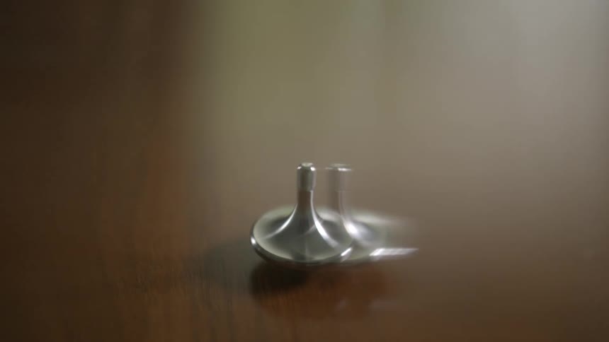 A close-up shot of a sleek metal spinning top rotating on a reflective dark wooden table
