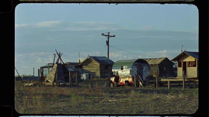 An eclectic collection of rustic wooden sheds and structures stands in a remote northern community under a blue sky