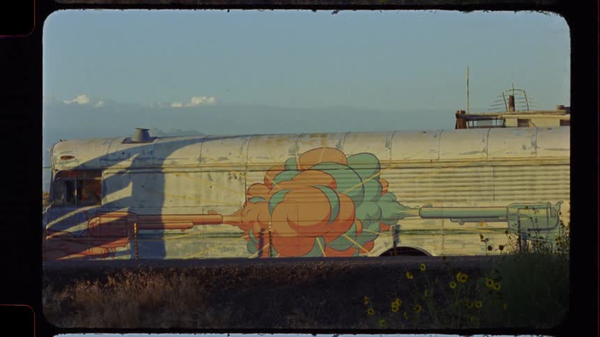Vintage film captures an abandoned bus with colorful graffiti art sitting in a sunny, rural field