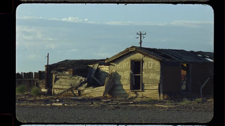An abandoned and crumbling wooden shack with a 'Private Property No Trespassing' sign sits in a desolate landscape in this vintage film footage