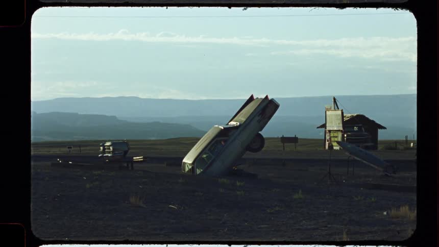 Surreal vintage film shot reveals a classic car buried nose-first in a desolate desert landscape