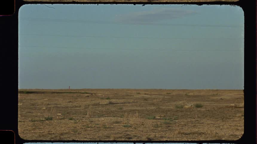 Vintage 8mm film transitions from a motion blur to a static wide shot of a vast, desolate, and arid landscape