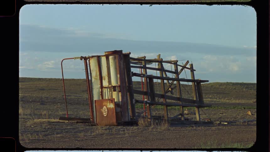 An old, forgotten fuel pump stands crooked and rusted in a desolate field under a pale sky