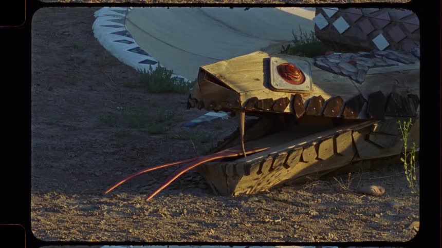 A rustic, wooden snake sculpture with a forked tongue sits in the golden hour light of a desert landscape, captured on vintage film