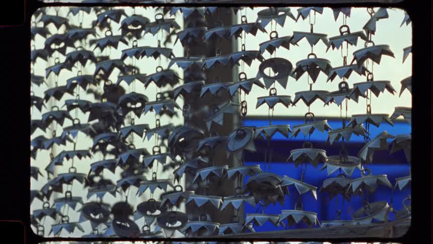 A static close-up shot of an abstract metal art installation featuring hanging eye-like shapes and jagged pieces, captured on vintage film
