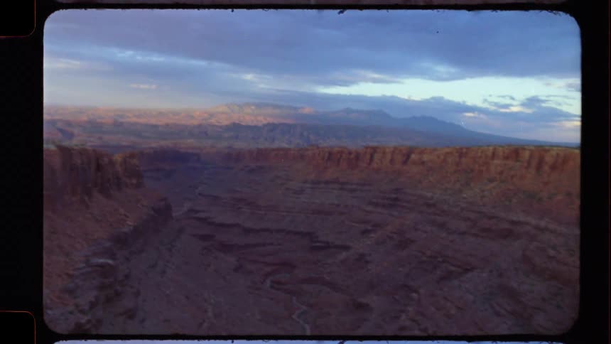 A vintage film shot pans across a majestic red rock canyon landscape under a dramatic, cloudy sky