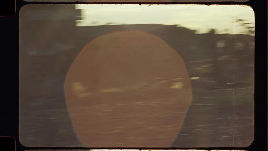 Vintage Super 8 film reveals a desolate junkyard with abandoned RVs behind a chain-link fence, filled with warm light leaks