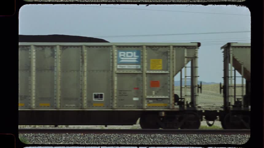 Authentic vintage film captures a long freight train with coal-filled hopper cars moving slowly across the tracks