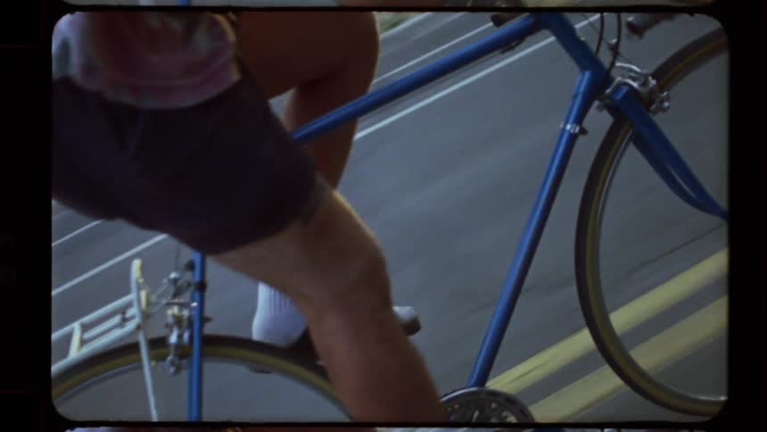 Close-up detail shot of a cyclist pedaling a blue road bike, captured on vintage film