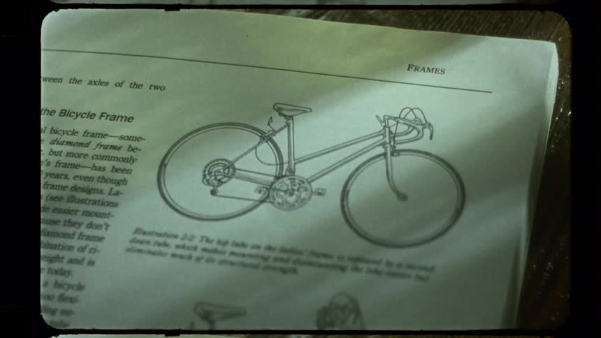 Flipping through a vintage bicycle manual to a diagram of a bike frame with a Super 8 film effect