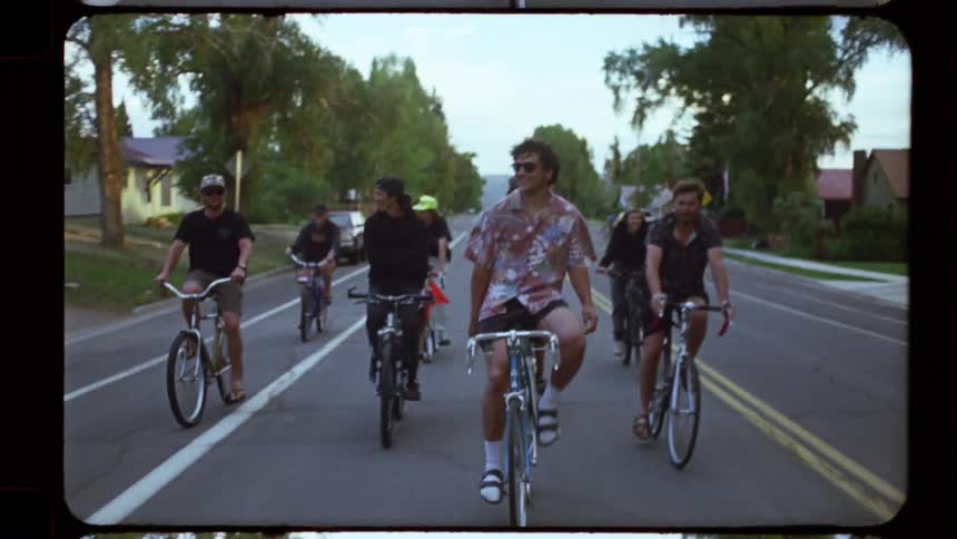Vintage-style slow-motion footage of a group of young friends casually riding their bikes down a neighborhood street at dusk