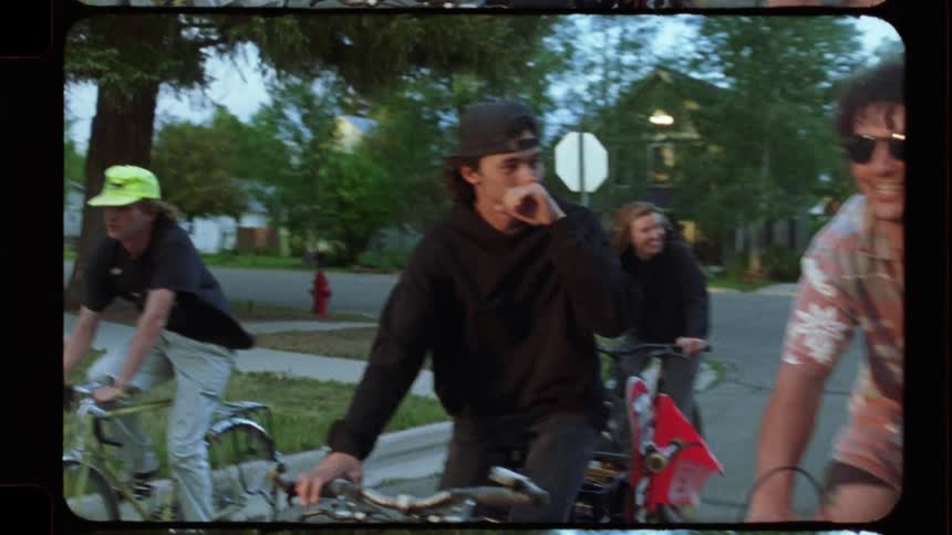 A group of diverse friends joyfully ride their bicycles together down a residential street in slow motion, shot on vintage film