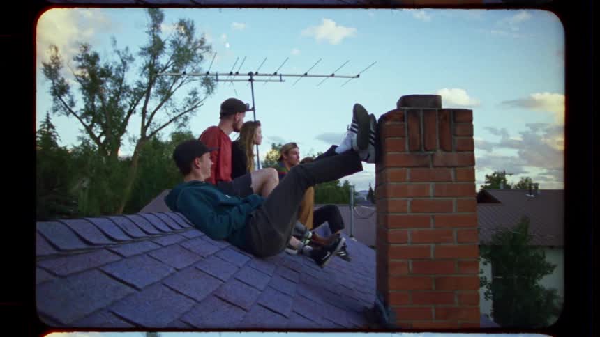 Carefree young friends laugh and hang out on a suburban rooftop in grainy, vintage-style footage