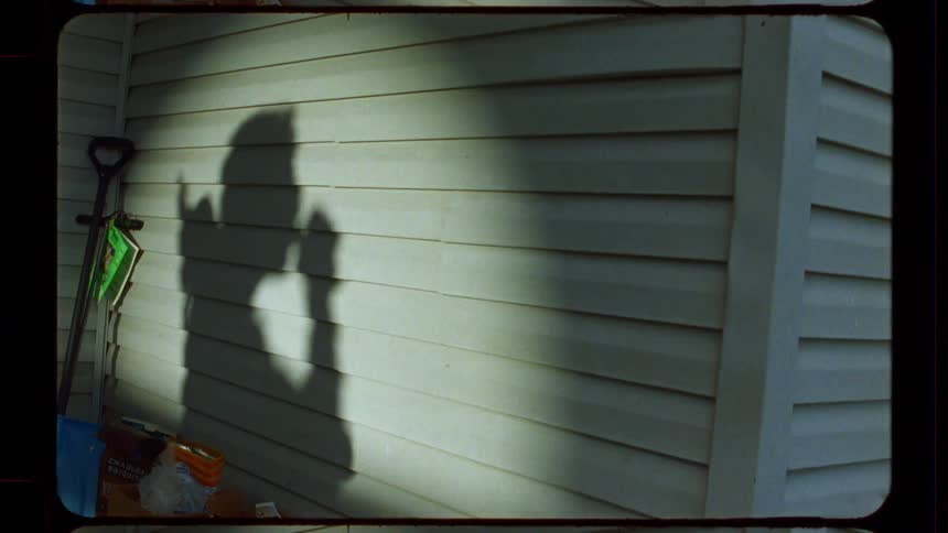 The shadow of a person drinking is cast on the vinyl siding of a house in this vintage Super 8 film clip
