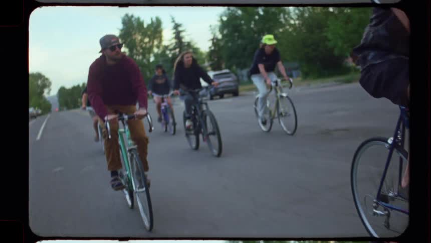 A group of friends enjoys a leisurely bike ride through a neighborhood on a sunny day in a retro film style