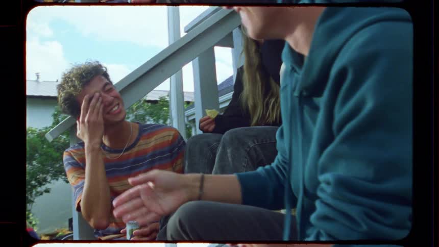 Vintage-style film captures a group of young friends laughing and talking while hanging out on the porch steps on a sunny day