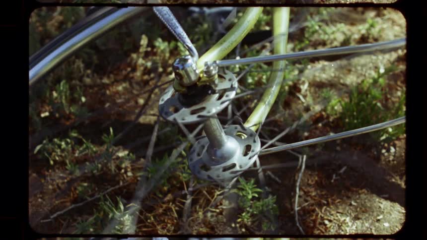 A close-up shot of a bicycle wheel spinning freely on a sunlit dirt path, captured on vintage film