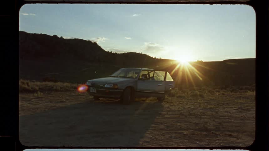 Authentic Super 8mm footage of an old car parked in a field with the door open during a vibrant sunset