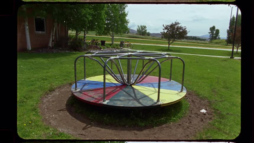 A colorful vintage merry-go-round spins rapidly in a park, creating a motion blur before coming to a slow stop