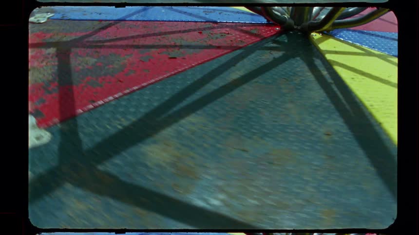 A close-up point-of-view shot from a colorful but weathered merry-go-round as it spins, captured on vintage 8mm film