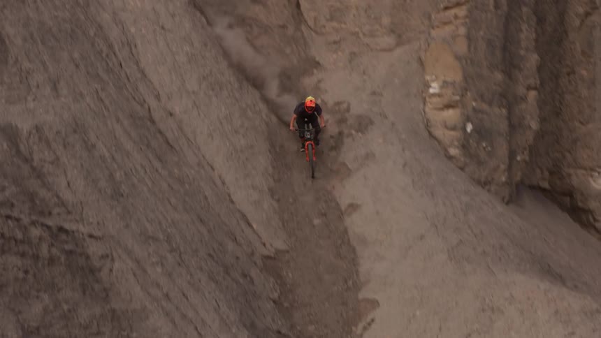 A skilled freeride mountain biker carefully navigates a treacherous and steep descent down a rocky desert canyon in slow motion