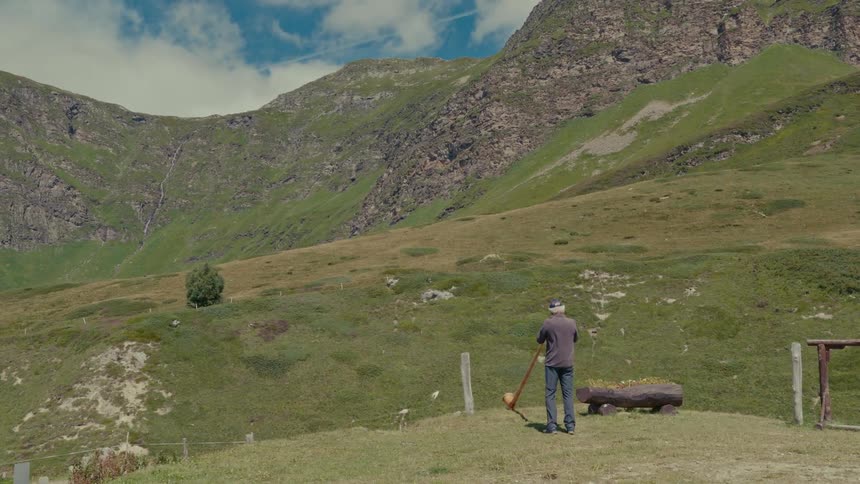A lone musician plays the traditional alphorn, its sound echoing through a vast green mountain valley