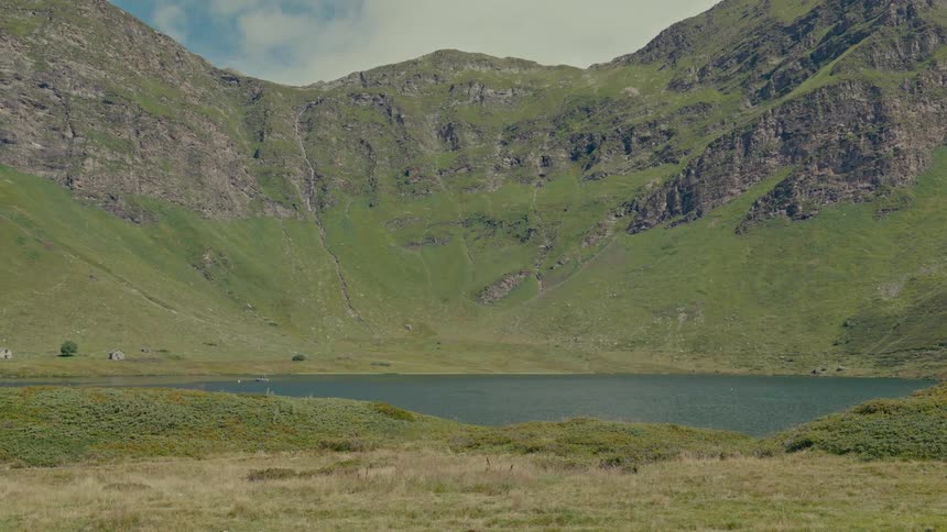 Static landscape view of a placid alpine lake at the foot of a verdant mountain range
