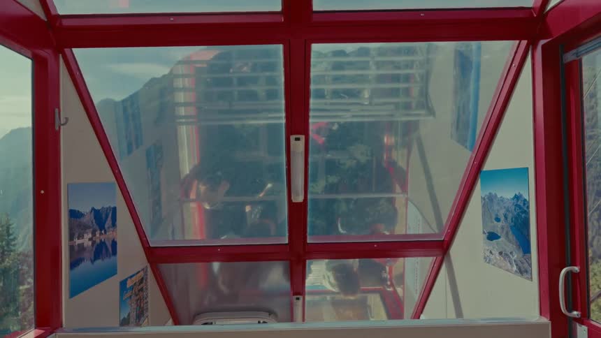 Interior view from a moving red mountain gondola showing passenger reflections on the window