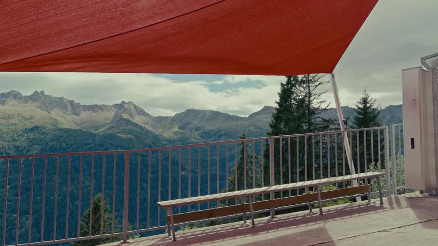 A quiet terrace with a bench and a red sunshade offers a scenic view of a majestic mountain range