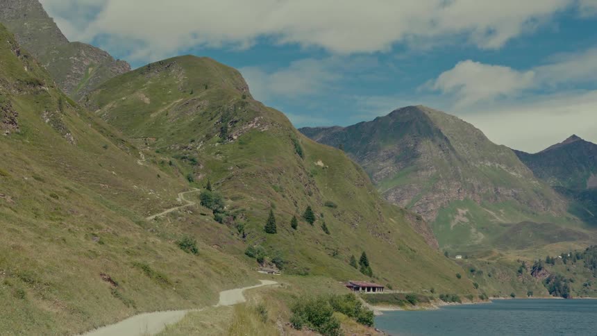 A serene mountain landscape featuring a winding dirt road alongside a tranquil lake under a blue sky with clouds