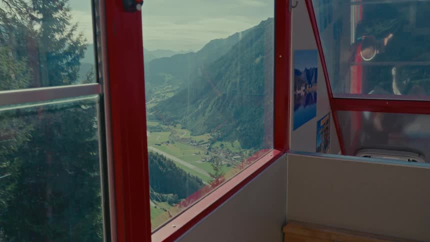 Scenic view from inside a red cable car descending into a lush mountain valley