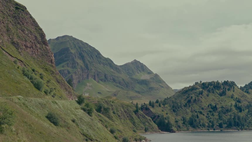 A serene view of a pristine lake nestled among lush green mountains under a cloudy sky