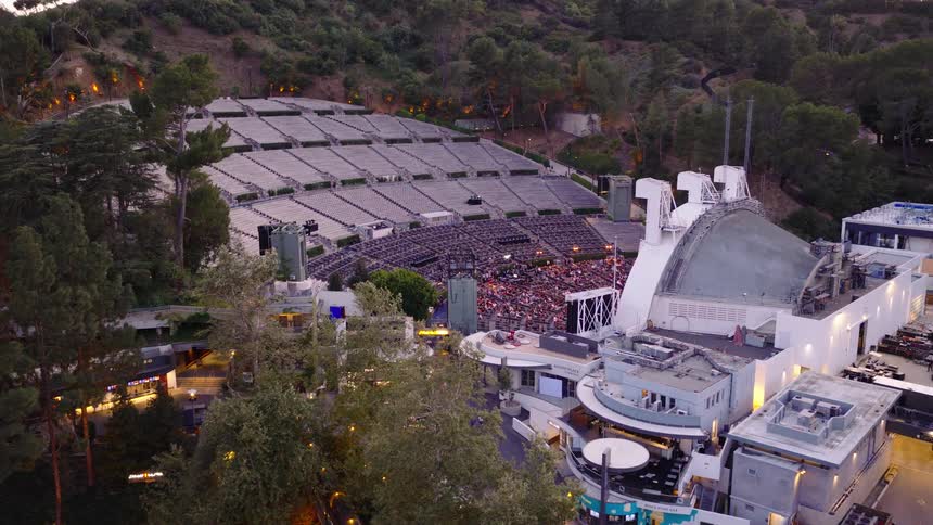 An aerial view slowly pushes in on the legendary Hollywood Bowl in Los Angeles, showcasing the crowd gathering for a concert at twilight