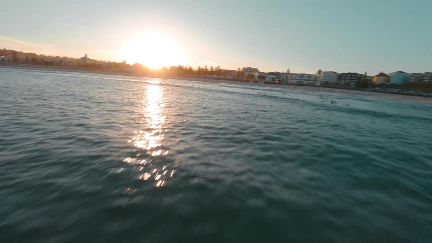 Dynamic FPV drone footage captures a stunning sunset flight over the waves and surfers at Bondi Beach