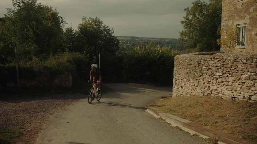 A female cyclist wearing a helmet smiles as she rides her bike up a winding country road in the late afternoon