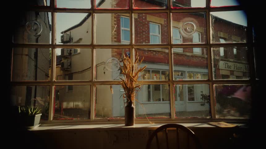 Two cyclists in athletic gear ride past a rustic window looking out onto a sunny town street