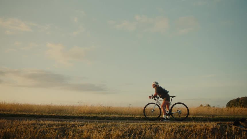 A woman in cycling gear sits on her bike in a field of golden grass against a soft sunset sky in this looping cinemagraph
