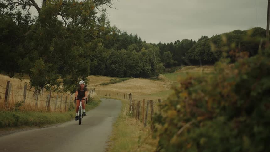 A female cyclist rides her bike along a quiet, scenic road in the rural countryside