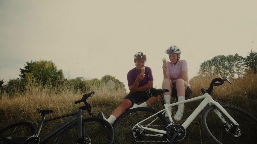 Two women on a bike ride take a joyful break, eating ice cream cones and laughing together in the countryside