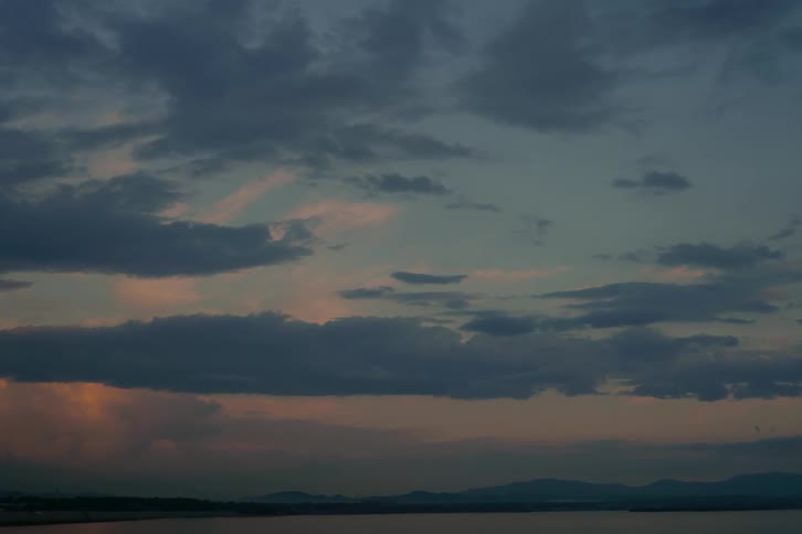 A moody, cloud-filled sky reflects the colors of twilight over a calm body of water