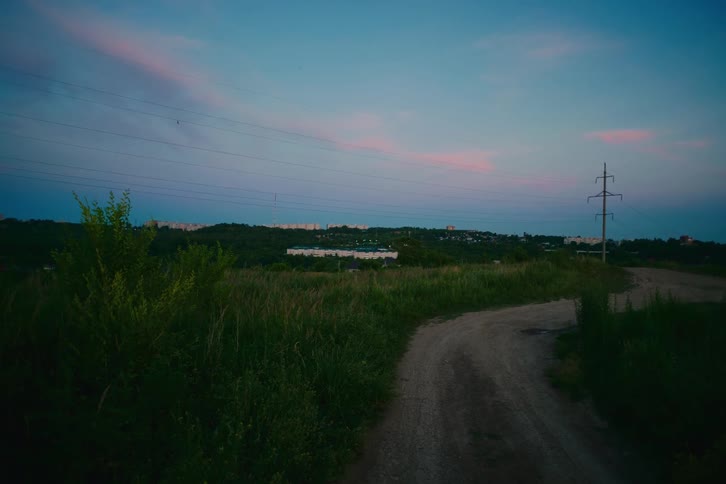 A serene view of a country dirt road leading towards a distant village at twilight
