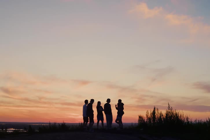 Silhouettes of a group of friends stand on a hilltop, enjoying the picturesque view of the colorful sunset