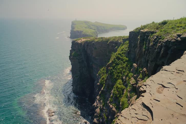 Majestic green cliffs drop sharply into the tranquil turquoise sea on a hazy summer day