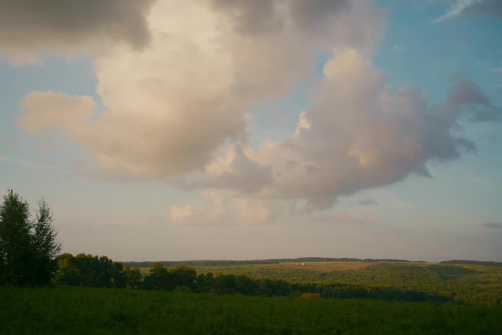 Vast, peaceful landscape of rolling green hills and forests under a beautiful sky with golden clouds at sunset