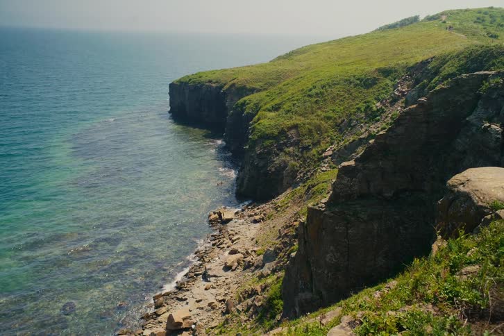 A serene view of a rocky coastline with lush green cliffs meeting the clear turquoise ocean on a sunny day